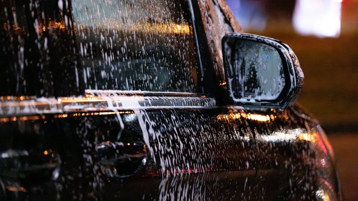 Black car being washed at night with city lights reflecting on glossy surface